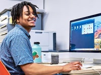 一位身穿蓝色衬衫坐在条记本电脑后面浅笑的年青人