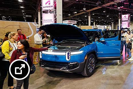 Blue electric pickup trucks on display at an indoor automotive event with attendees nearby.