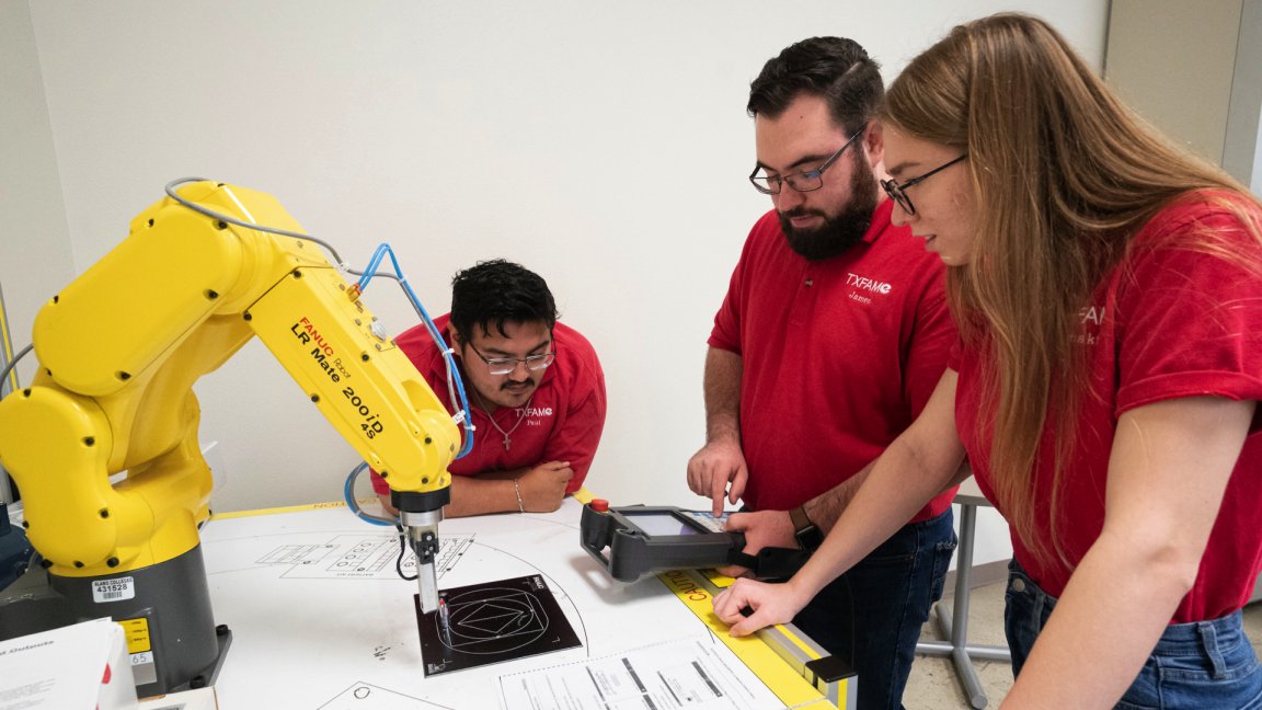 Students standing over and tinkering with robotics and hydraulics  machines while learning at St. Philips College. 