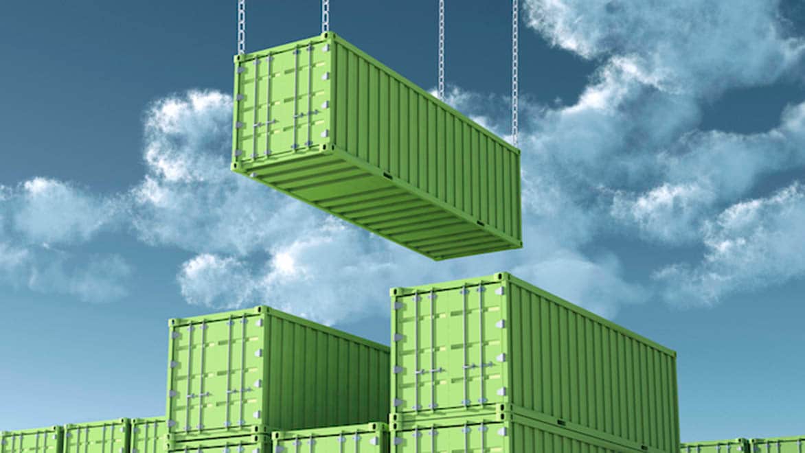 A shipping container is lowered onto a stack of shipping containers.