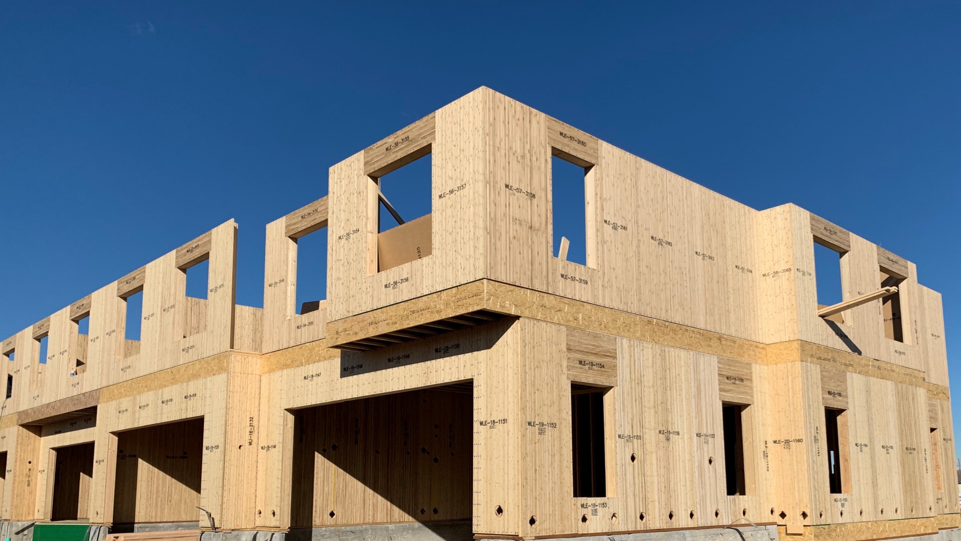 Ground view of the corner of an in-progress townhome construction project with exposed BamCore panels. Clear blue sky background.