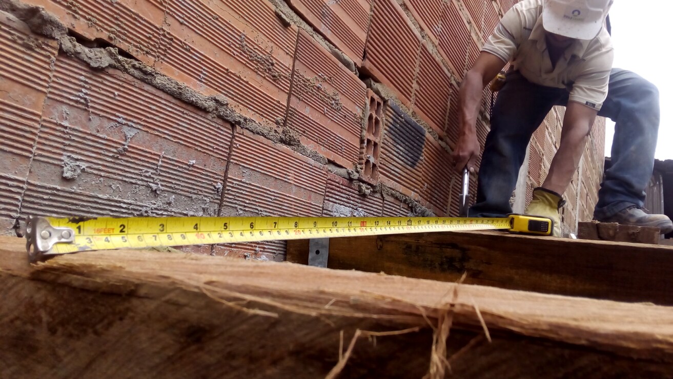 Worker measuring steps with a tape measure at a Build Change construction site.