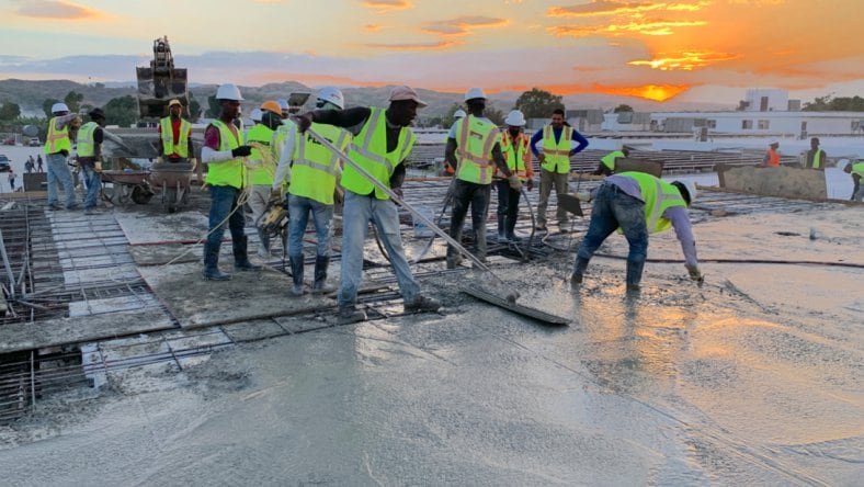 A group of workers wearing high-viz vests and jeans pouring and leveling cement at Build Health International construction site.