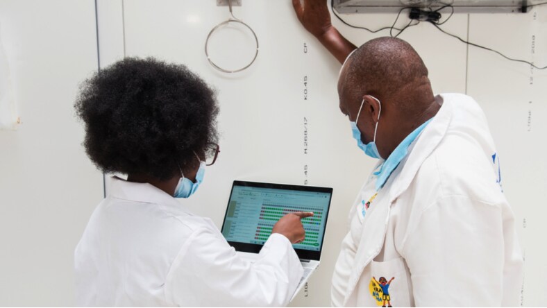 Two medical personnel examining Nexleaf Analytics data on a laptop screen next to a white wall.