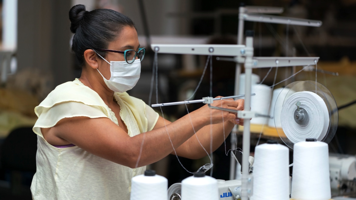Woman wearing mask and glasses operating a textile spooling machine.