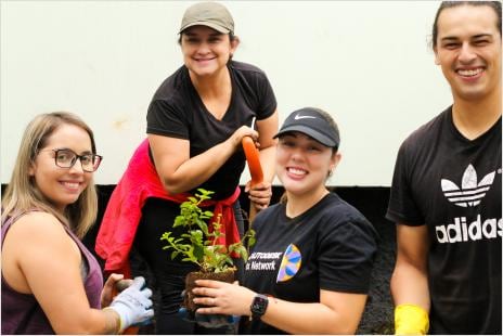 Four smiling Autodesk Costa Rica employees in casual clothes holding a potted plant, participating in a volunteer event.