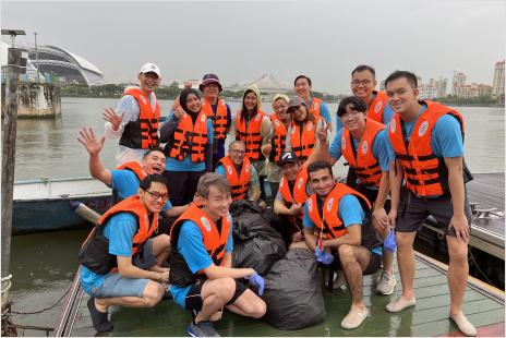 Group of Autodesk Singapore employees wearing life vests posing on a dock with large trash bags, participating in a waterfront cleanup activity.
