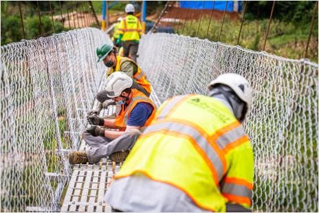 Bridges to Prosperity team members installing fencing on a suspension bridge in rural Rwanda.