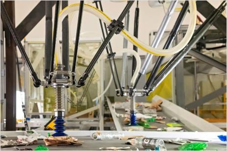 Automated robotic arms equipped with suction cups sorting recyclable materials on a conveyor belt in a recycling facility.