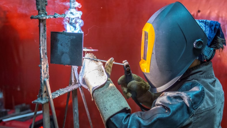 A person wearing a welding mask and gloves welding a metal object.