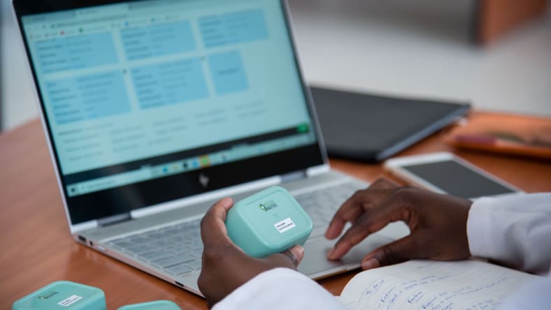 Two hands holding medical data devices in front of a laptop.