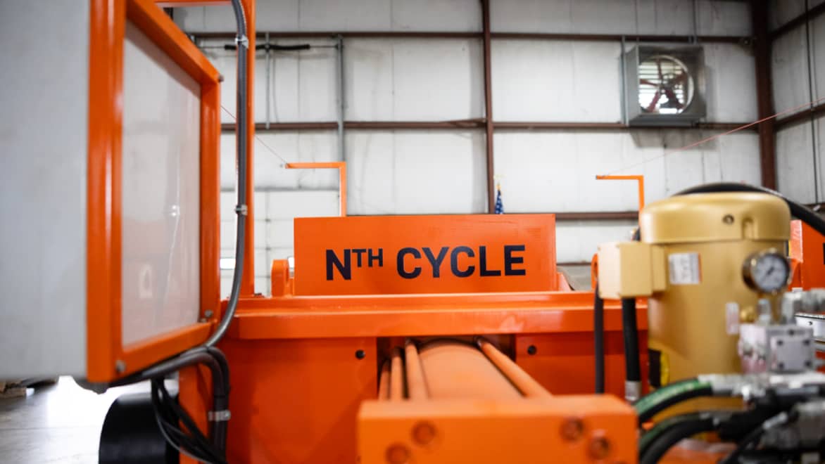 Side view of Nth Cycle "OYSTER" electro-extraction machine. The machine is highlighter orange with a prominent "Nth Cycle" logo, located in a large warehouse space.