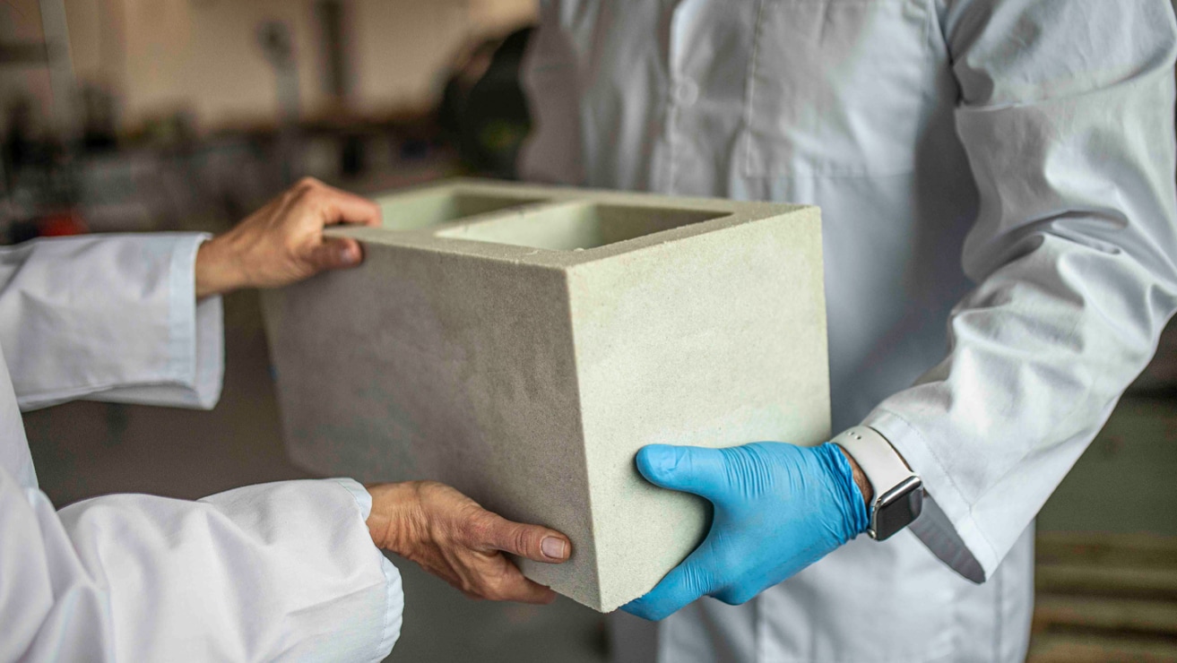 A Prometheus Materials employee wearing blue latex gloves passing a bio-cement block to another employee.