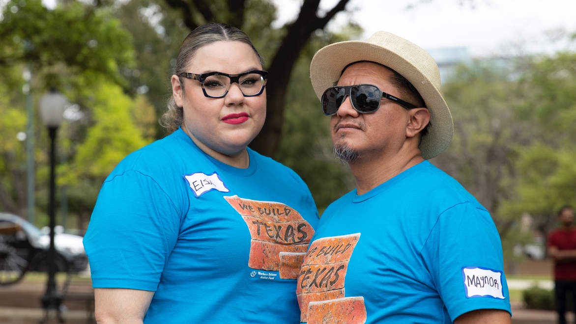 Families and workers from Better Builder (FWF grantee) in Austin, Texas — Two individuals standing side-by-side: Individual on the left is wearing glasses and a blue logo shirt with a nametag, looking into camera; individual on the right is wearing sunglasses and a tan brimmed hat, looking into the distance.