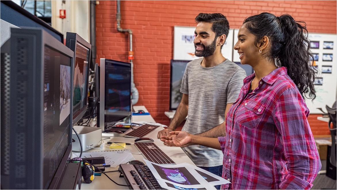 Two animators in a film studio stand in front of monitors, working on animations.
