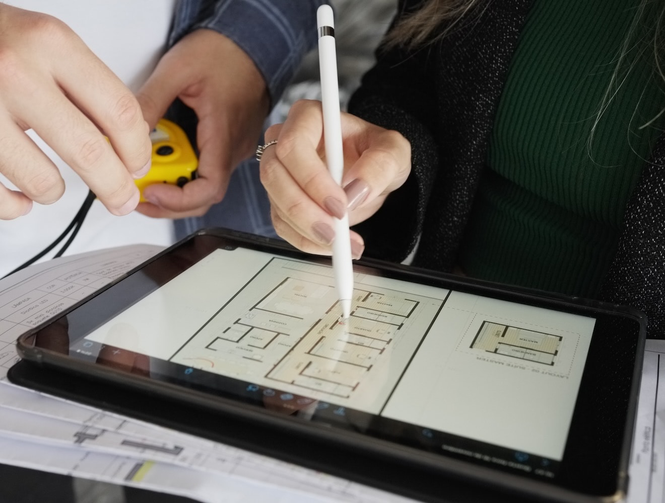 A close-up photo shows two architects making notes on a blueprint drawing on digital tablet.