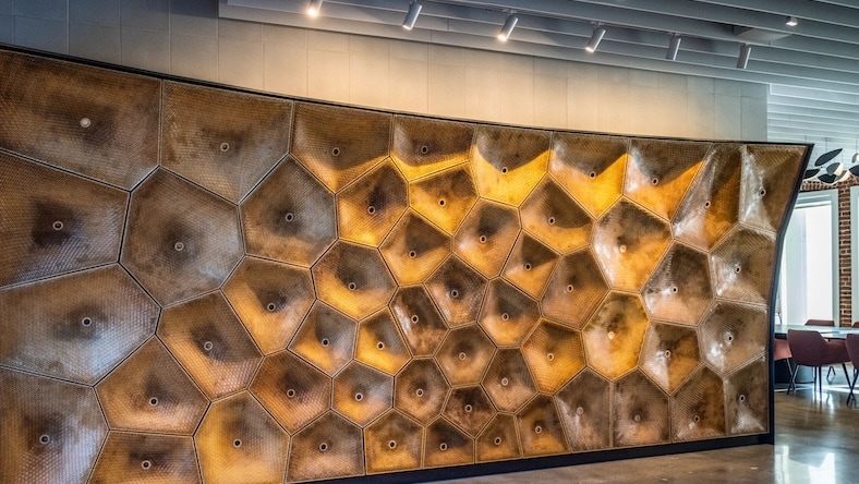 A large wood sculpture on the wall of an office building is illuminated by track lighting.