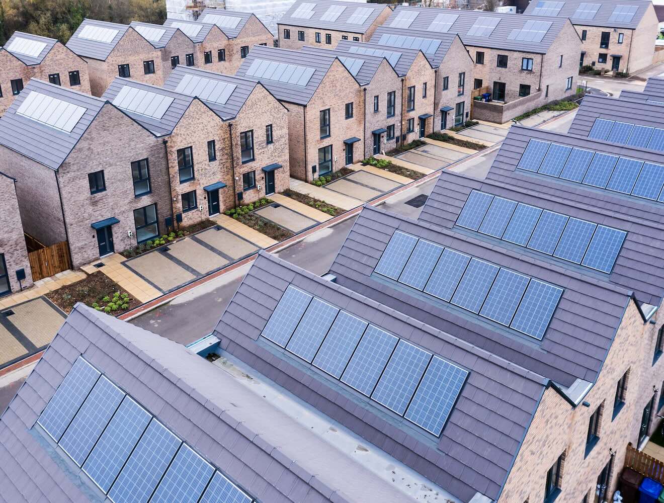 An aerial view shows rows of energy-efficient modular homes with rooftop solar panels.