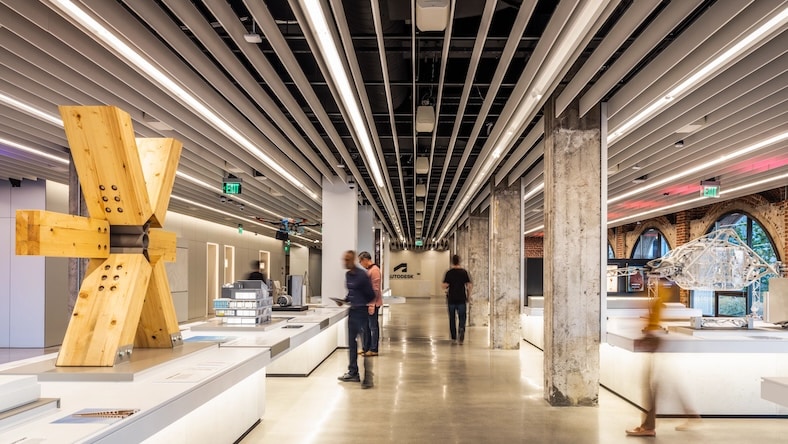 The interior of an art gallery showcases several types of ambient lighting, including ceiling lights, light from windows, downlights, and reflections off the polished floor.