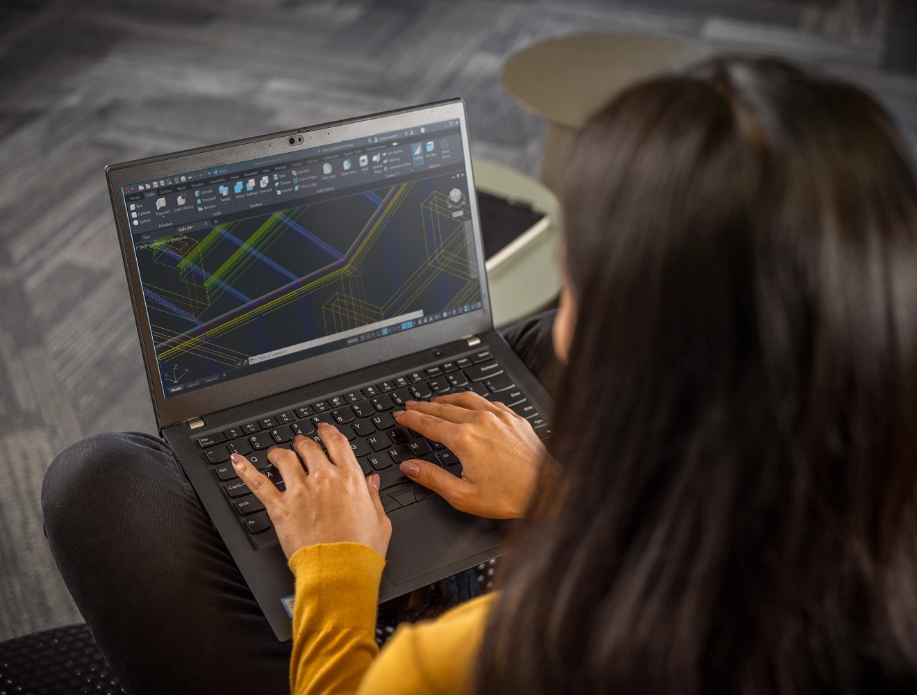 A close-up of a woman’s hands shows her working in AutoCAD on a laptop.