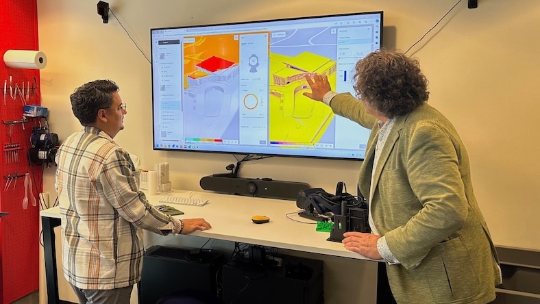 Two men stand next to a wall-mounted screen displaying a Forma analysis