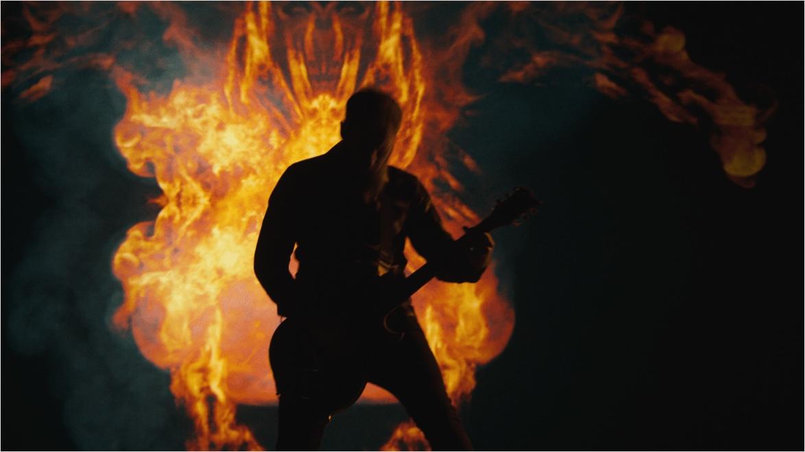 Guitarist of Tenside shreds in front of a demon made of fire in a still from the "Shadow to Shine" music video.