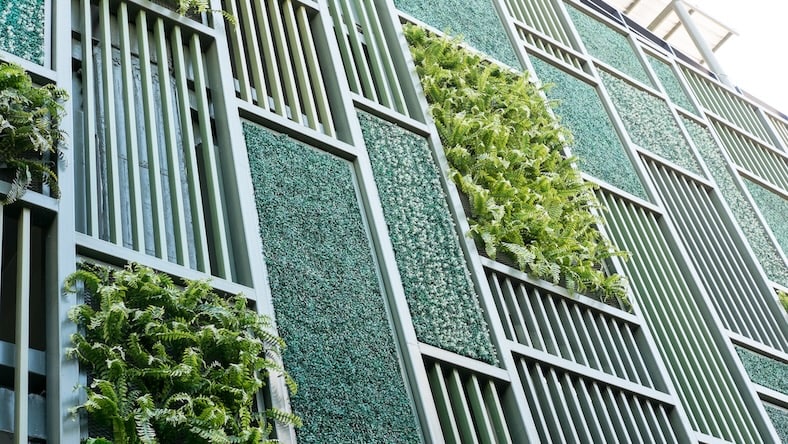 504647142 A building is clad in a green facade featuring plant-filled panels.