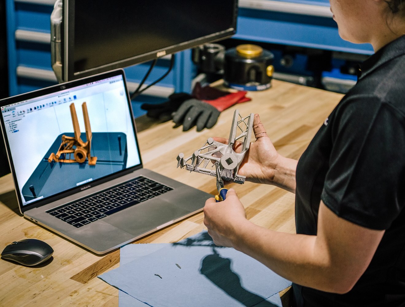 A woman holds a 3D printed object and looks at a laptop displaying the object's design in Fusion.