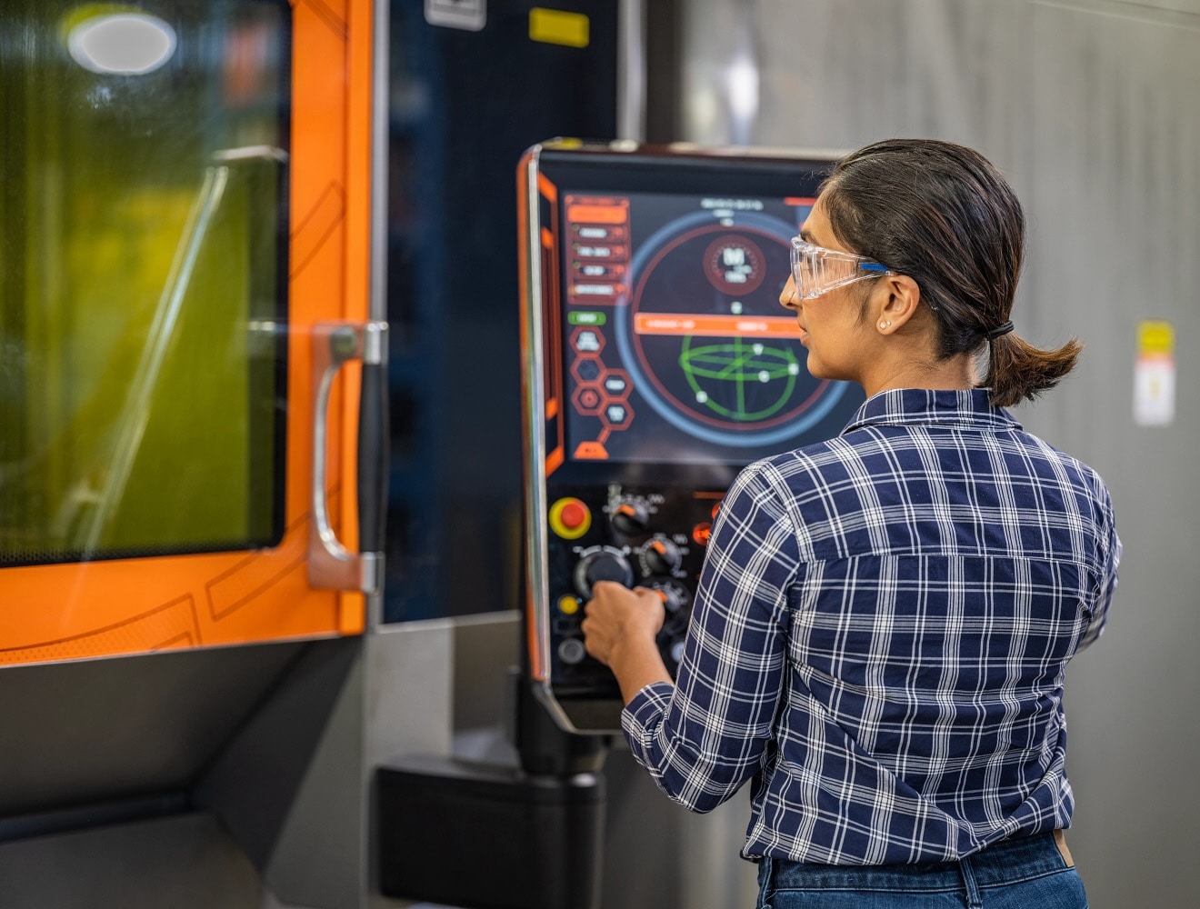 A woman operates a CNC machine in a machine shop.