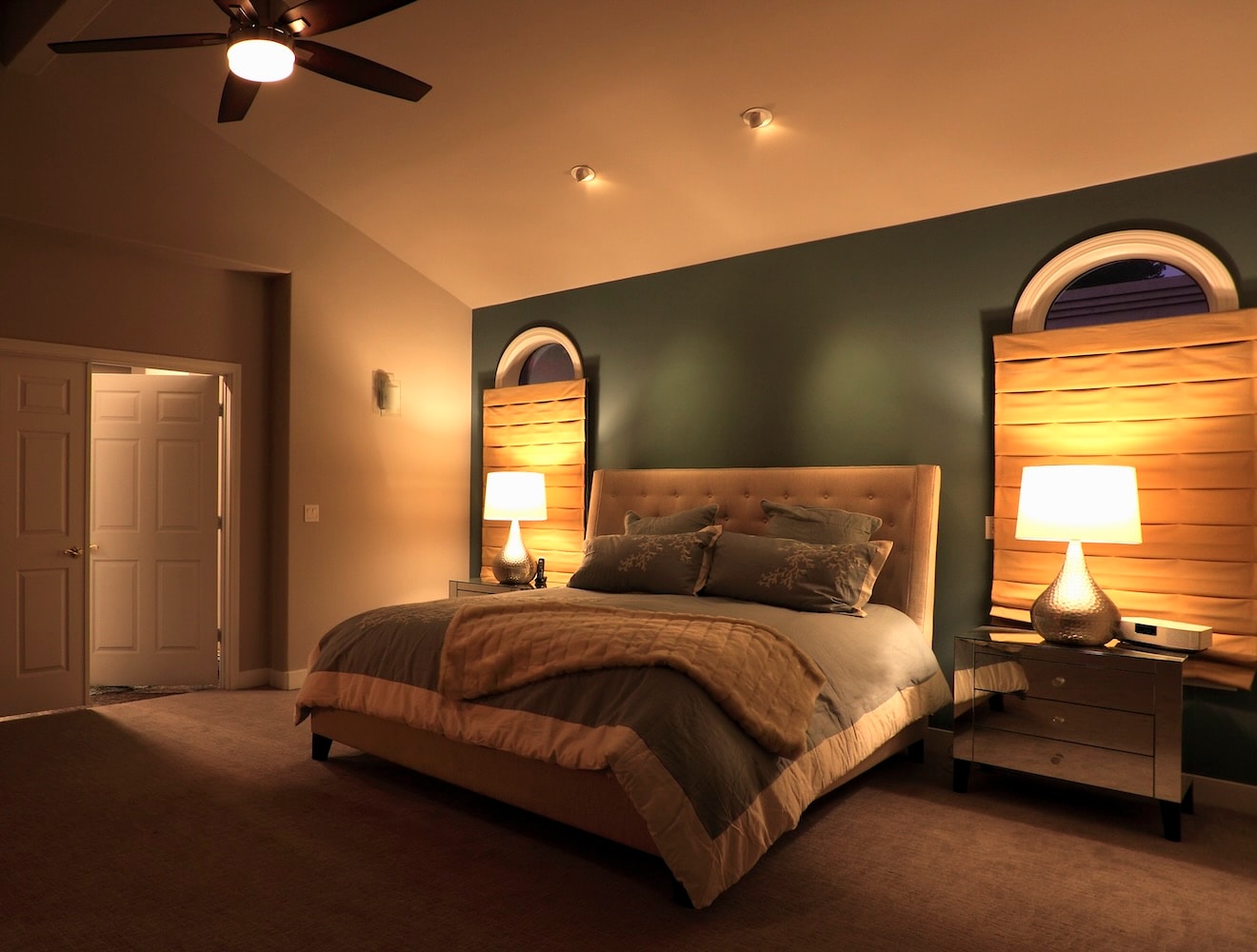 A large bedroom with high ceilings, carpeting, and warm, cozy lighting.