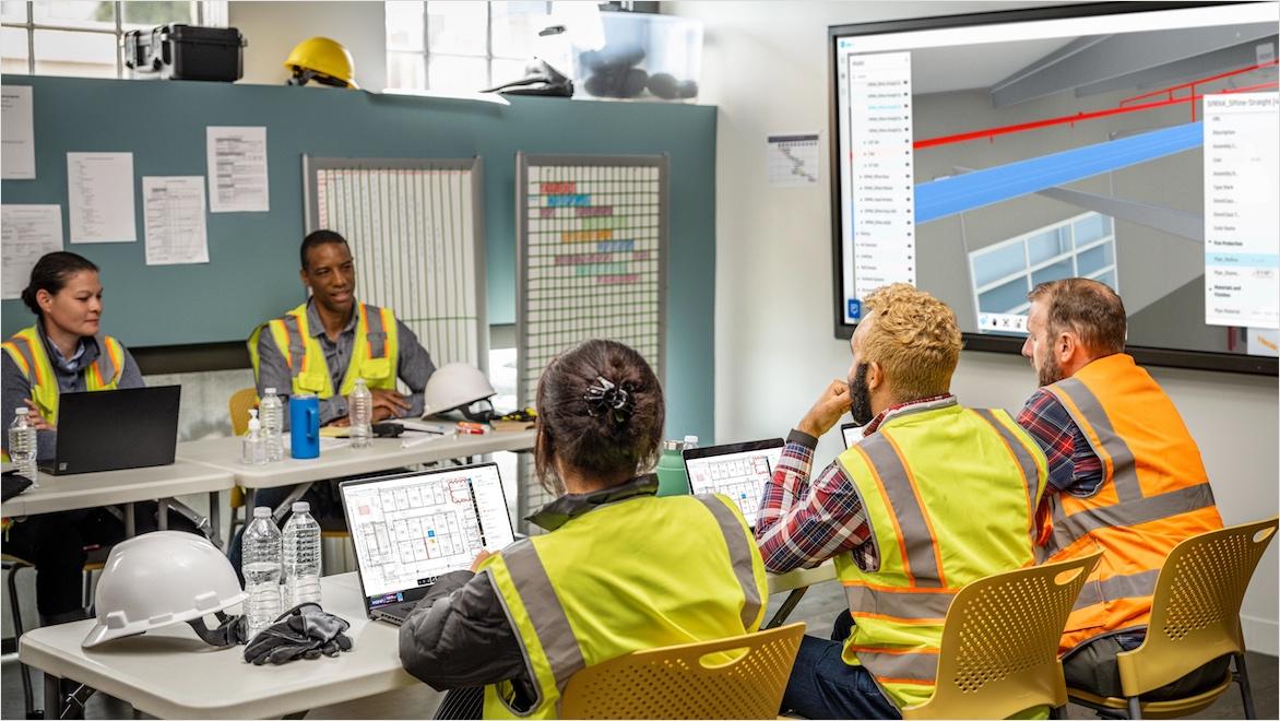 Five construction workers sit inside a job trailer during a meeting.