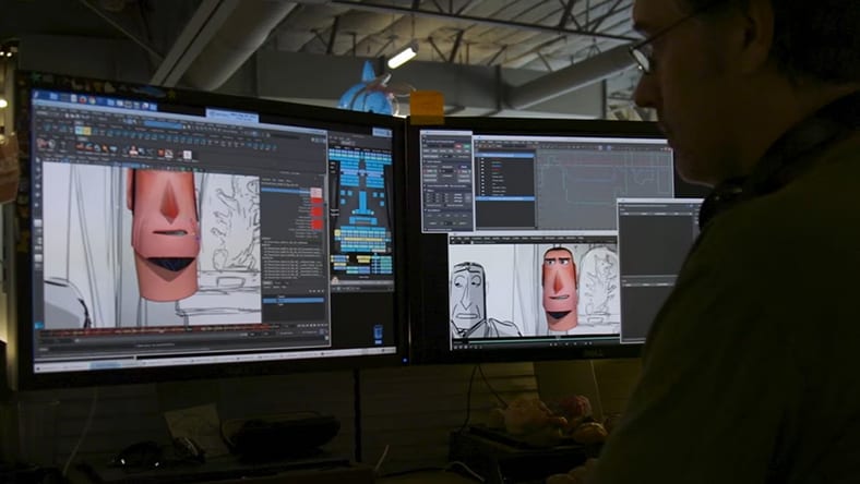 An animator works at dual monitors displaying 3D character modeling software with close-ups of a character's face.
