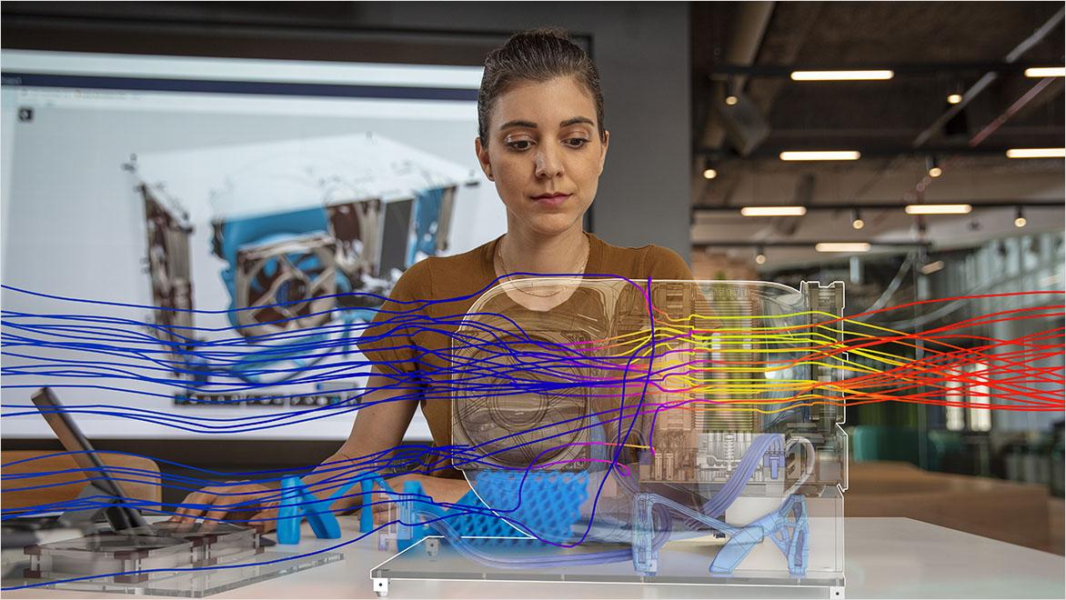 A woman analyzes a digital simulation of airflow over a machine prototype displayed with colorful flow lines in a modern office environment. 