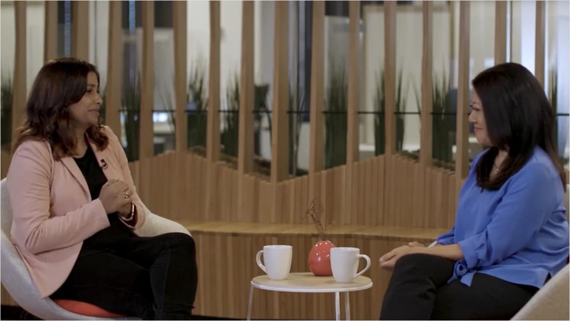 Two women sit in chairs, facing each other and speaking.