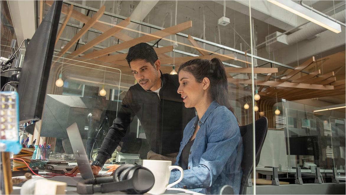 A man and woman collaborate on a laptop in an industrial office setting