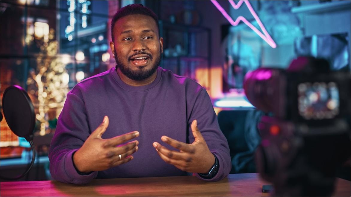 A man sits at a desk in front of a camera, producing a podcast.