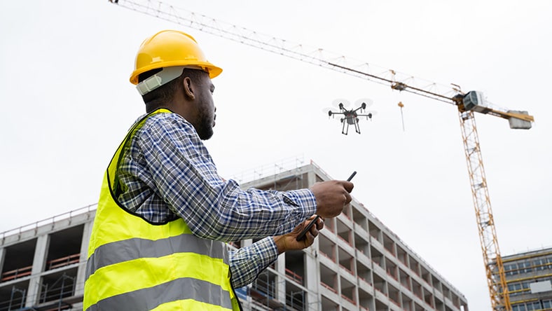 A construction worker in a hard hat pilots a drone.