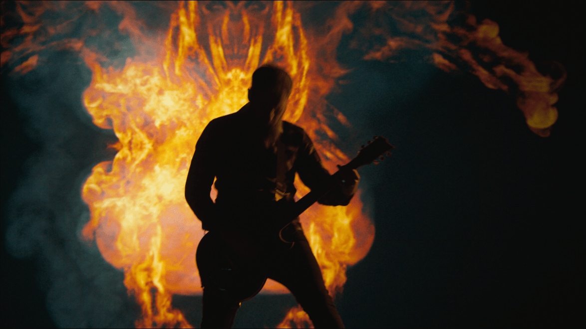 Guitarist of Tenside shreds in front of a demon made of fire in a still from the "Shadow to Shine" music video.