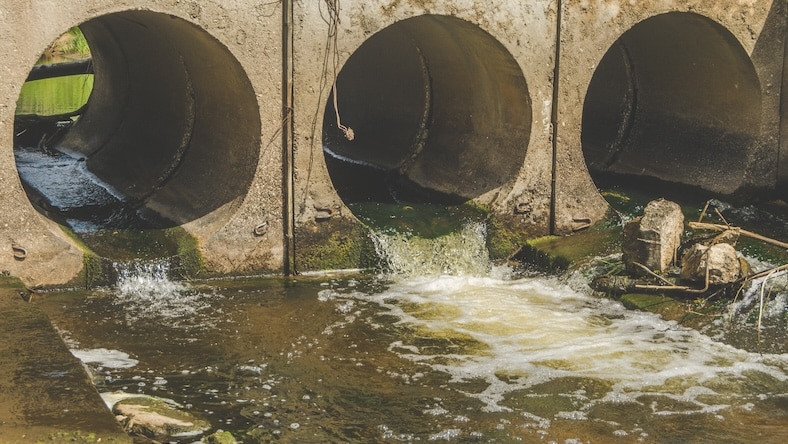 Turbid water flows from drainage pipes into a river.