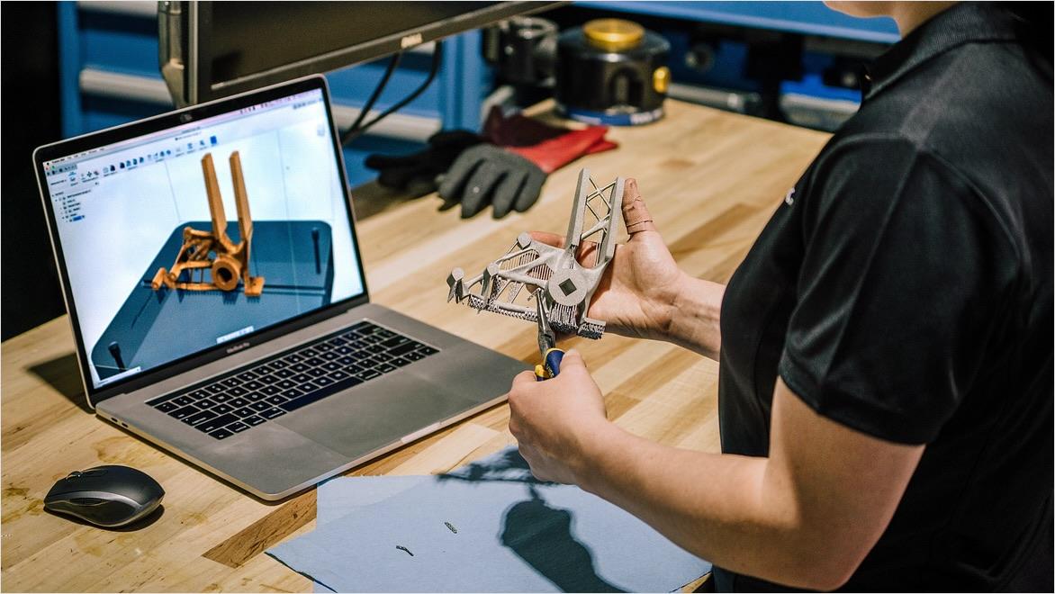 A woman looks at a laptop displaying CAM software while holding a prototype of the design on the screen.