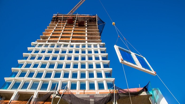 Workers consult plans while standing on a concrete foundation. 
