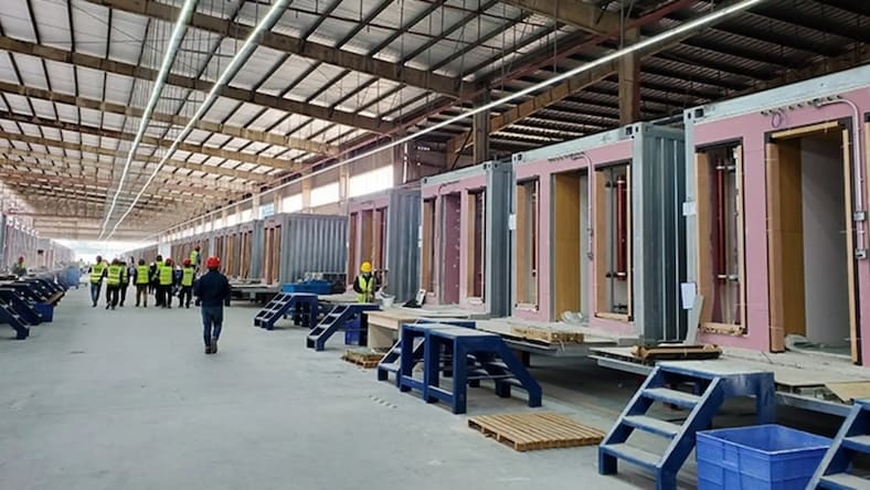Unfinished housing modules are lined up on a factory floor.