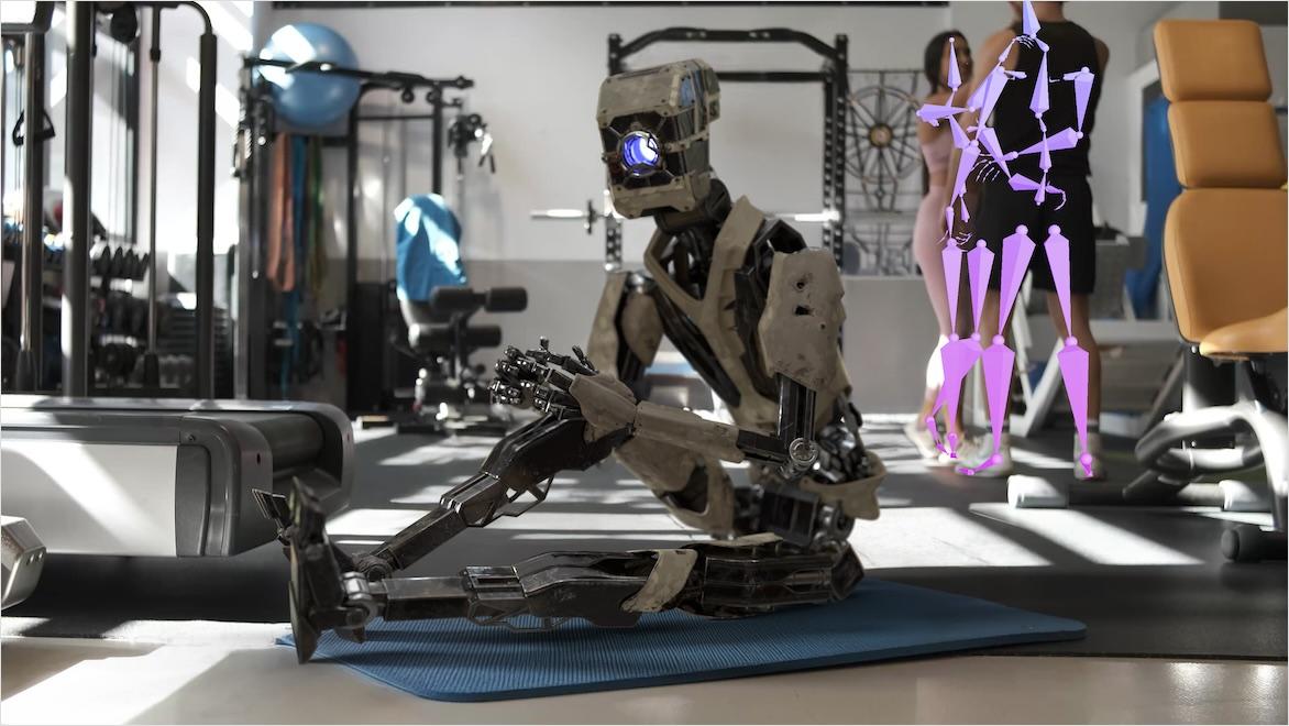 A robot character sits on a mat in an exercise room; two people behind him have rigging overlays indicating markerless motion capture.