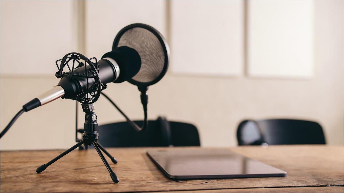 A microphone and pop shield on a stand sits on a table next to a laptop.
