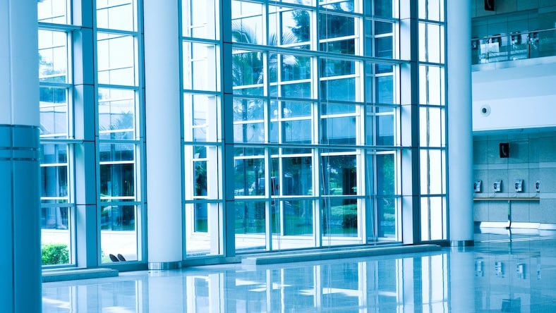 A modern building interior features floor-to-ceiling windows and a light, reflective floor.