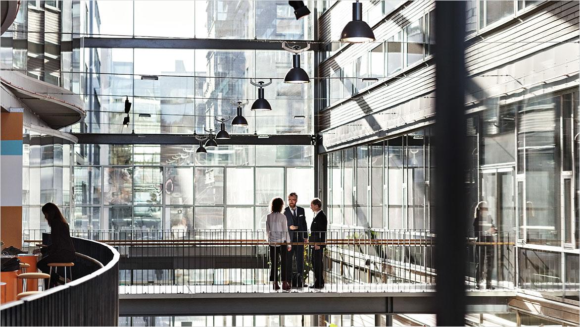 Three business colleagues stand together in a sunny office atrium.