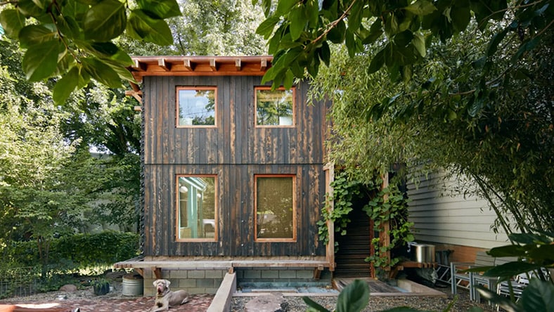 A small house with wood exterior sits on a lush green lot.