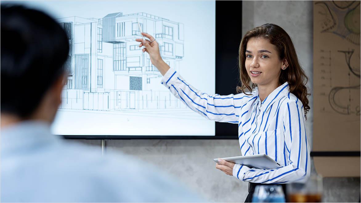 An architect shows a client a building model on a screen.