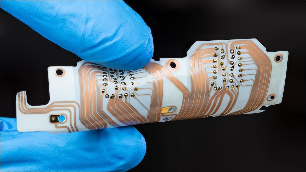 Flexible printed circuit board being held between two gloved fingers.