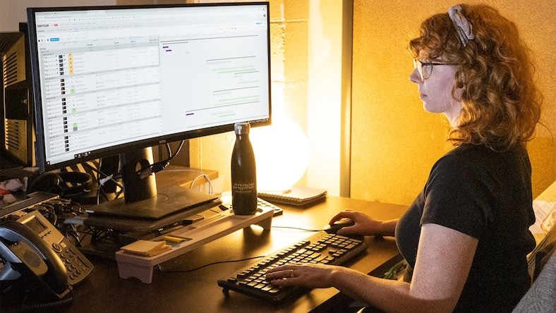 Woman seated at desktop computer displaying a project management screen